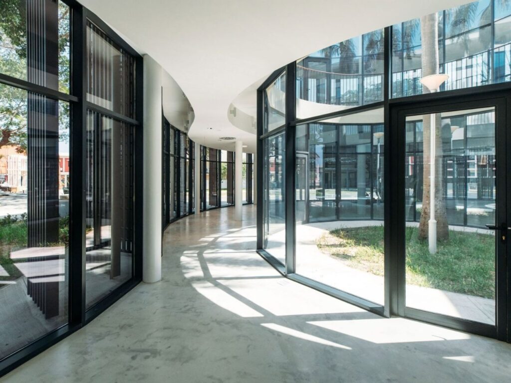 Curved interior hallway of Luanda Library flanked by full-height glass walls facing a planted patio.