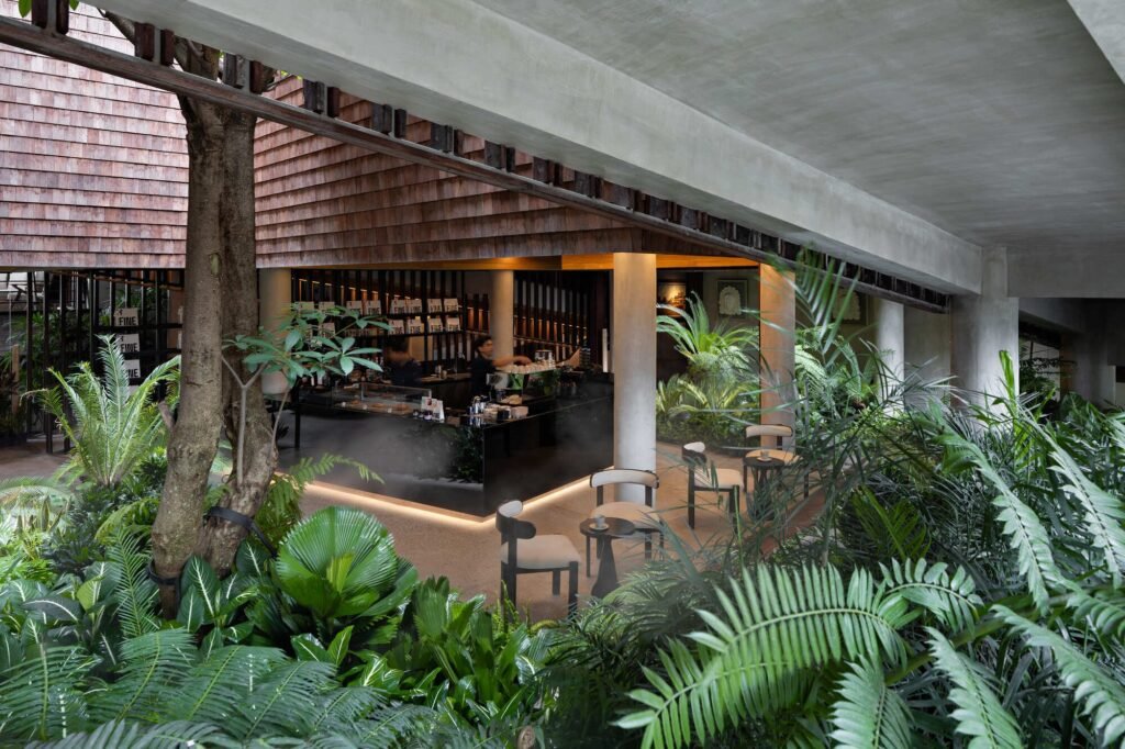 Coffee counter inside Kemilu Ubud enclosed by dense tropical vegetation, indoor trees, and exposed concrete structural beams.