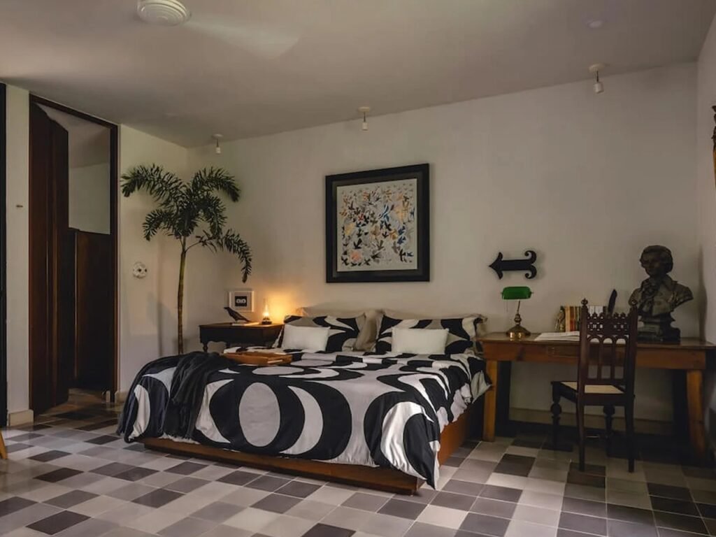 Bedroom with patterned black-and-white bedding, checkered floor tiles, custom study desk, and indoor palm tree at Casa del Loro.