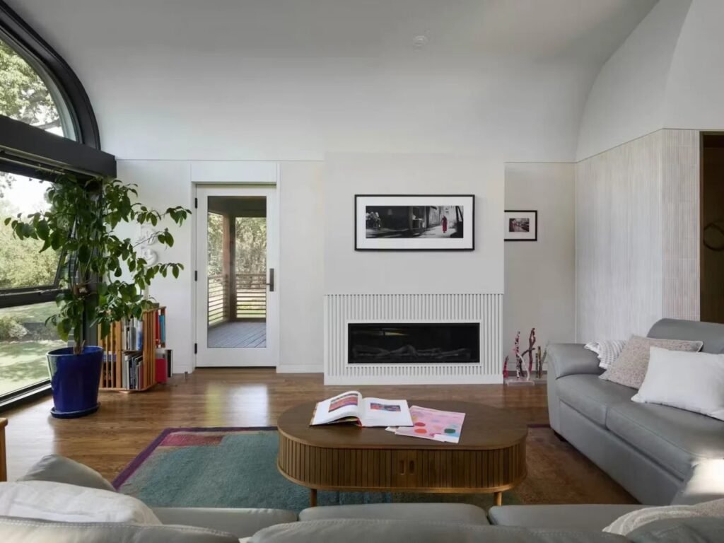 Modern fireplace wall in living room with white slatted surround, surrounded by hardwood flooring and natural sunlight.