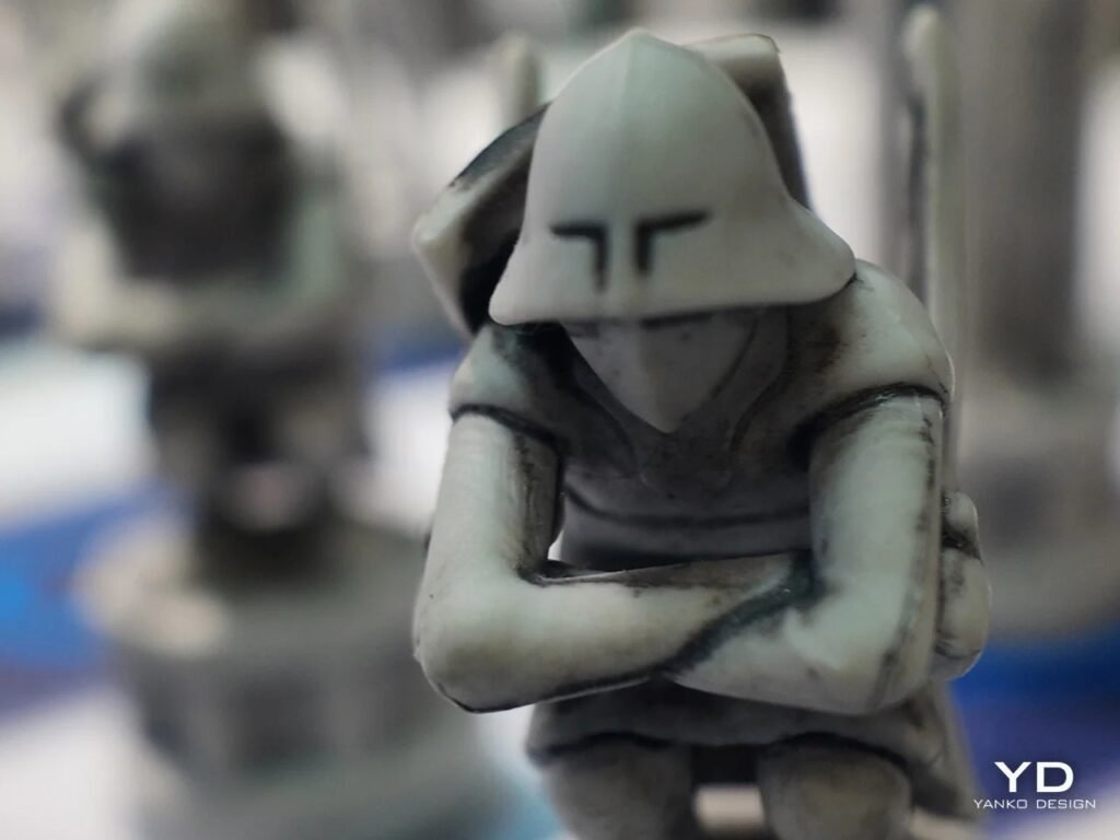 Macro close-up of a light-colored crouching pawn figure with a helmet and crossed arms.