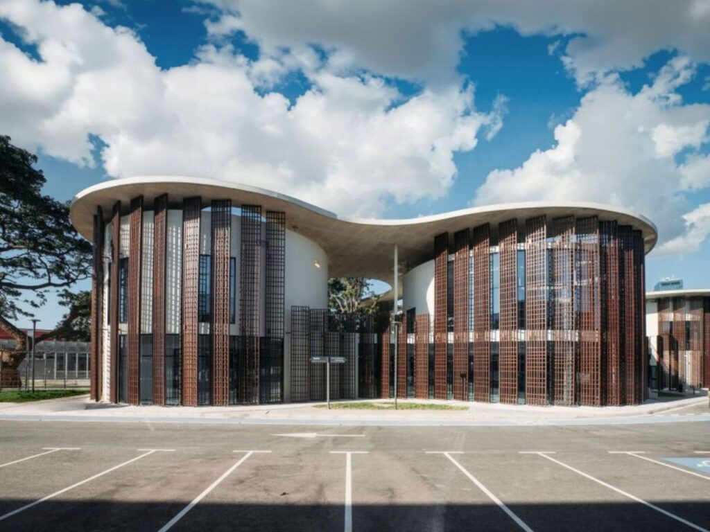 Street-level view of the undulating facade of Luanda Library featuring full-height timber shading louvers.