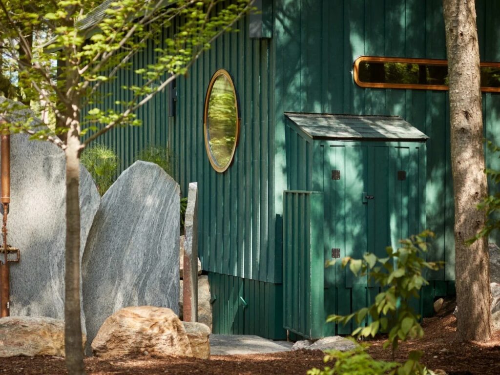 Exterior detail of green timber siding, round window frame, and natural granite rock landscaping.