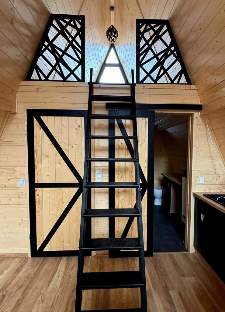 Black vertical wooden ladder positioned in front of sliding wooden barn doors and decorative black laser-cut loft privacy screens.