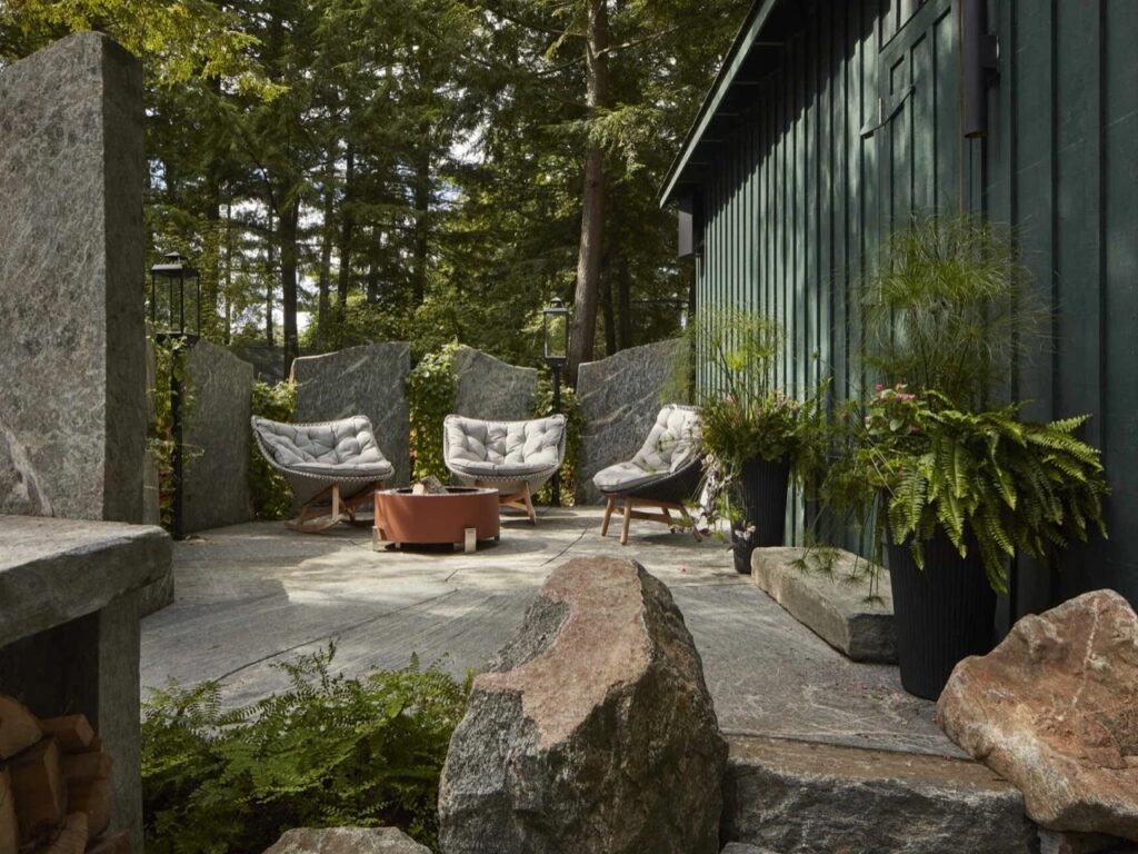 Outdoor stone patio lounge area with fire pit, rocking chairs, and granite retaining slabs.