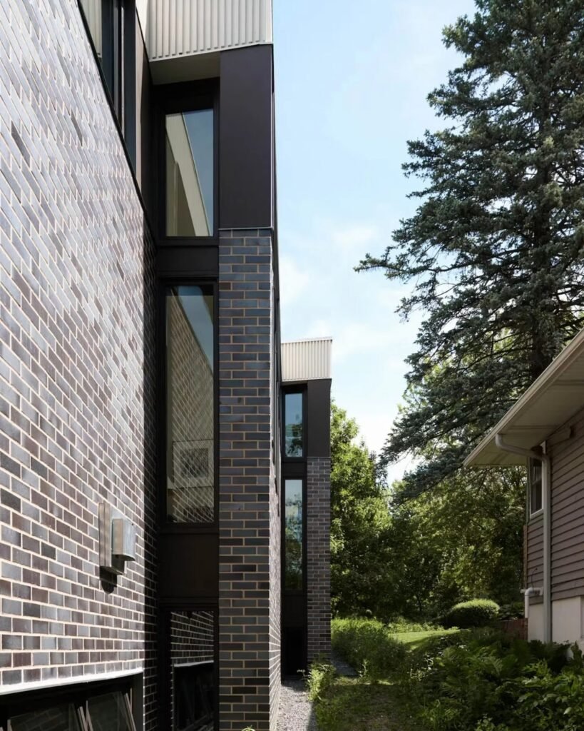 Vertical side facade of Crescendo house by CityDeskStudio featuring dark brick masonry and narrow linear windows.