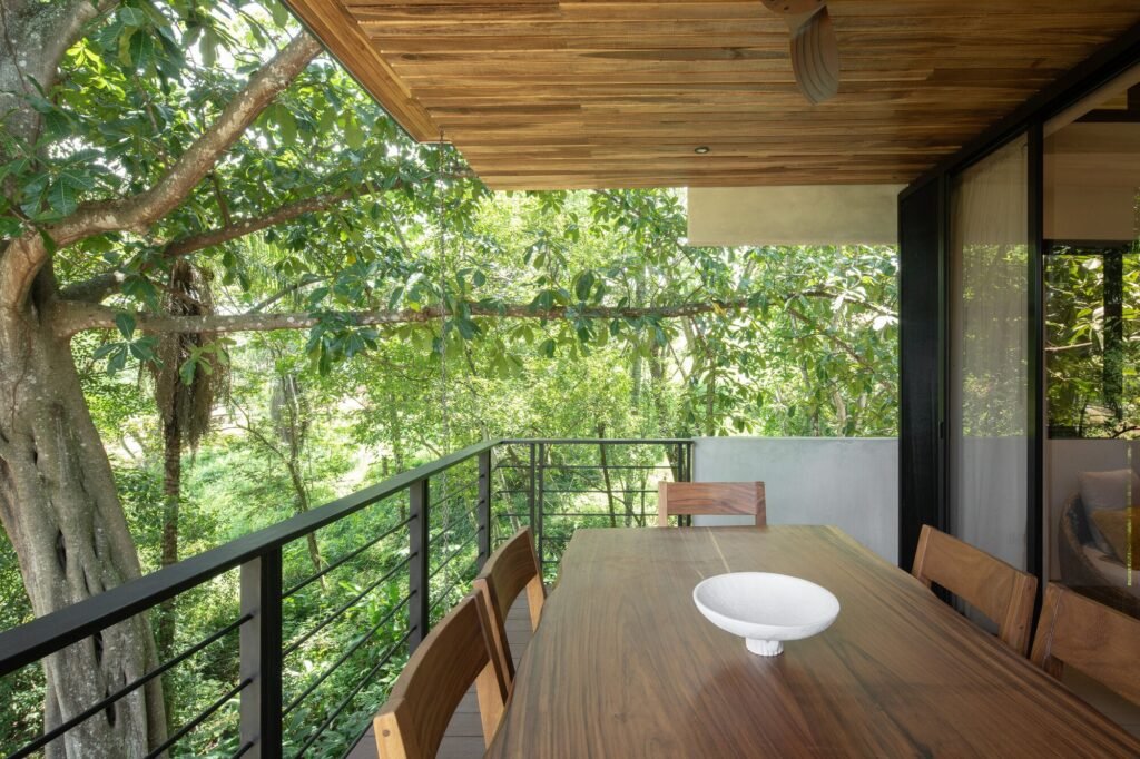 Outdoor wooden dining table on a covered balcony positioned directly next to a large native tree trunk.