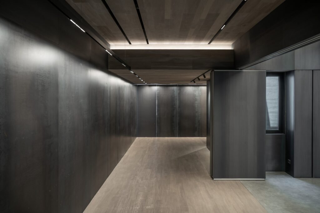 Dark narrow hallway with continuous linear track lights and polished stone floor.