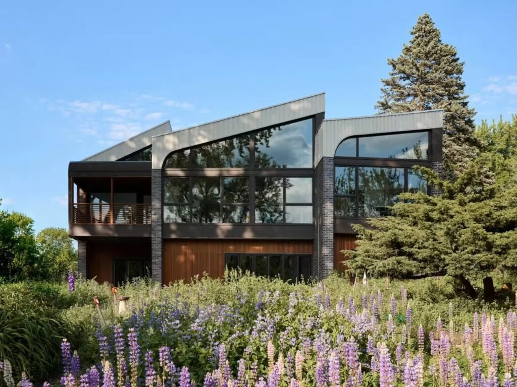 Daylight view of the rear elevation of Crescendo house showing stepped roof profile, glass wall openings, and purple wildflower lawn.