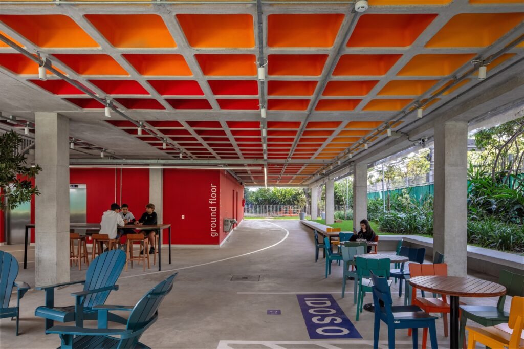 Covered ground floor gathering space with colorful waffle slab ceiling, red accent walls, and informal student seating.
