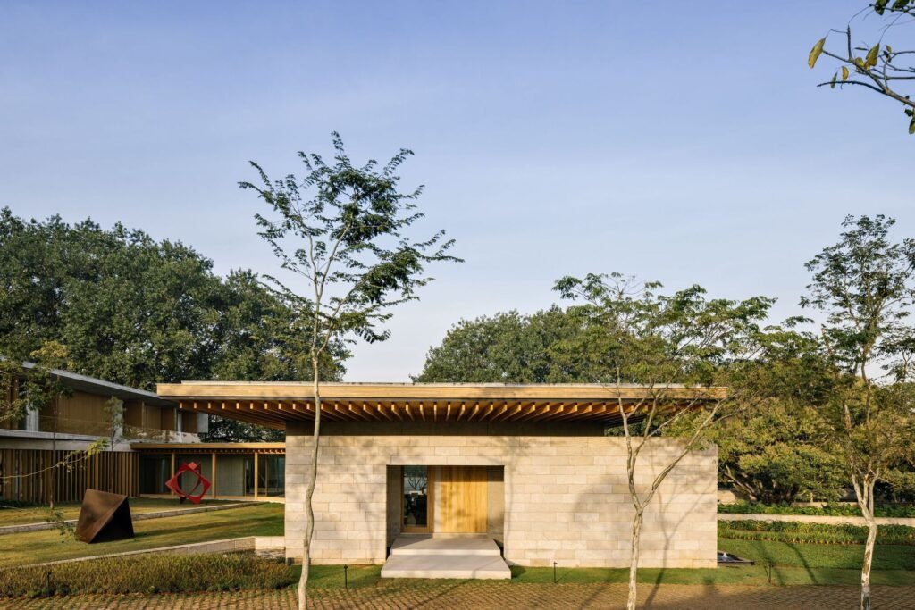 Stone volume with timber slatted overhang and outdoor sculptures set in a landscaped courtyard.