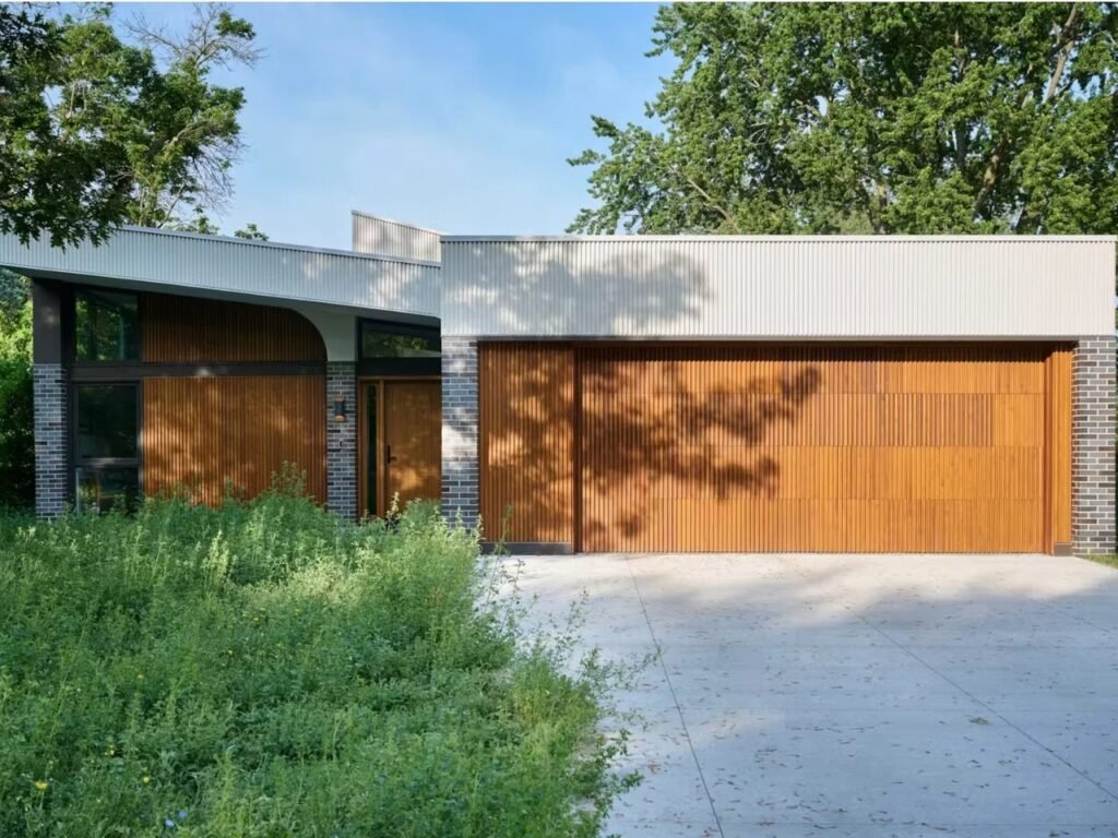 Front street view of Crescendo home showing a vertical wood-slatted garage door, concrete driveway, and low-slung roofline.