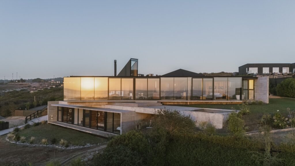 Twilight elevation view of Casa 22 built into a hillside, showcasing illuminated glass upper levels and a concrete lower level.