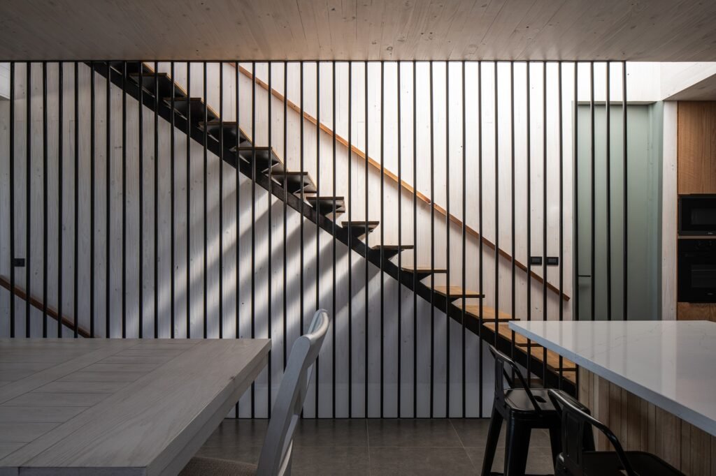 Interior detail of a sleek steel vertical slat screen and floating wooden staircase inside Gandarillas House.