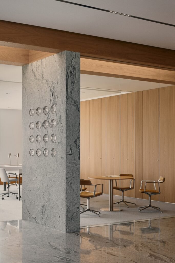Rough gray stone wall partition adjacent to glass walls, wood cabinetry, and a small discussion area with brown leather chairs.