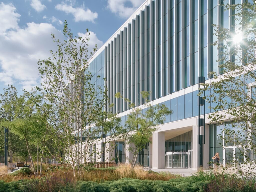 Low-angle perspective of glazed facade and vertical fins of Temple Quarter Enterprise Campus behind lush green arrival trees.