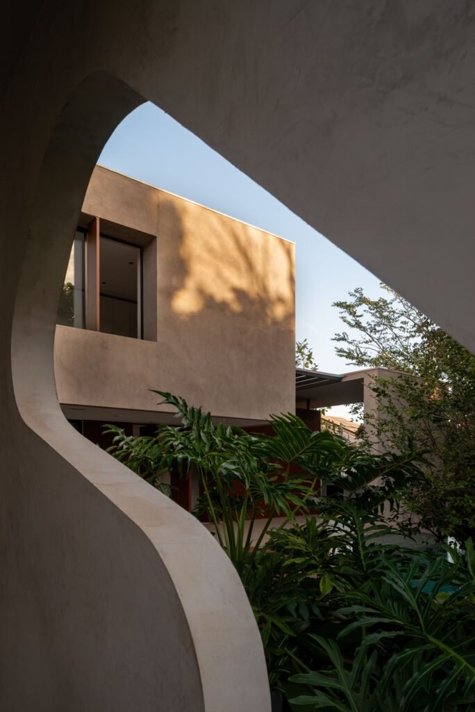 Frame view through an organic curved concrete opening looking towards the upper floor wall of Casa Noor.