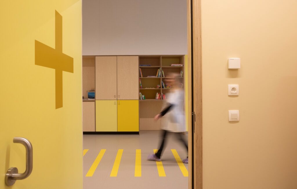 Bright hallway interior showing yellow wall signage, light wood cabinetry, and motion-blurred person walking.