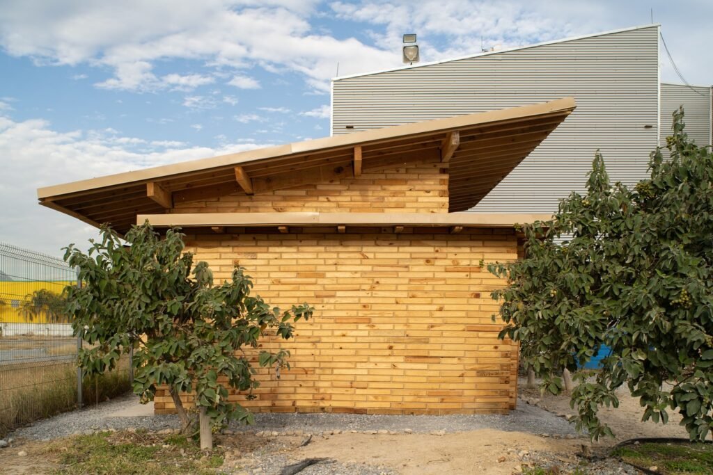 Straight-on view of the solid wooden block facade of La Grieta Pavilion framed by green foliage.