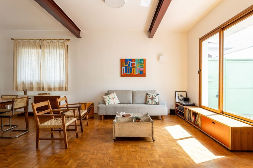 Living room with restored wooden parquet flooring, exposed steel I-beams, neutral sofa, and large sliding window with natural sunlight.
