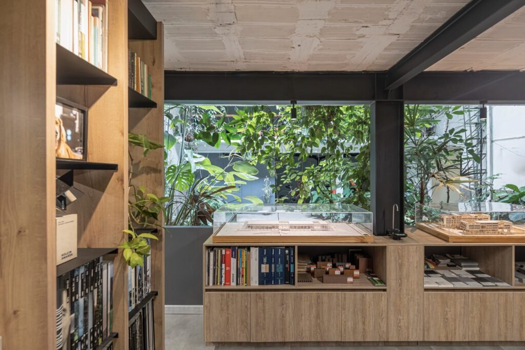 Custom wooden bookcase and storage unit with architectural scale models looking out toward green courtyard views.