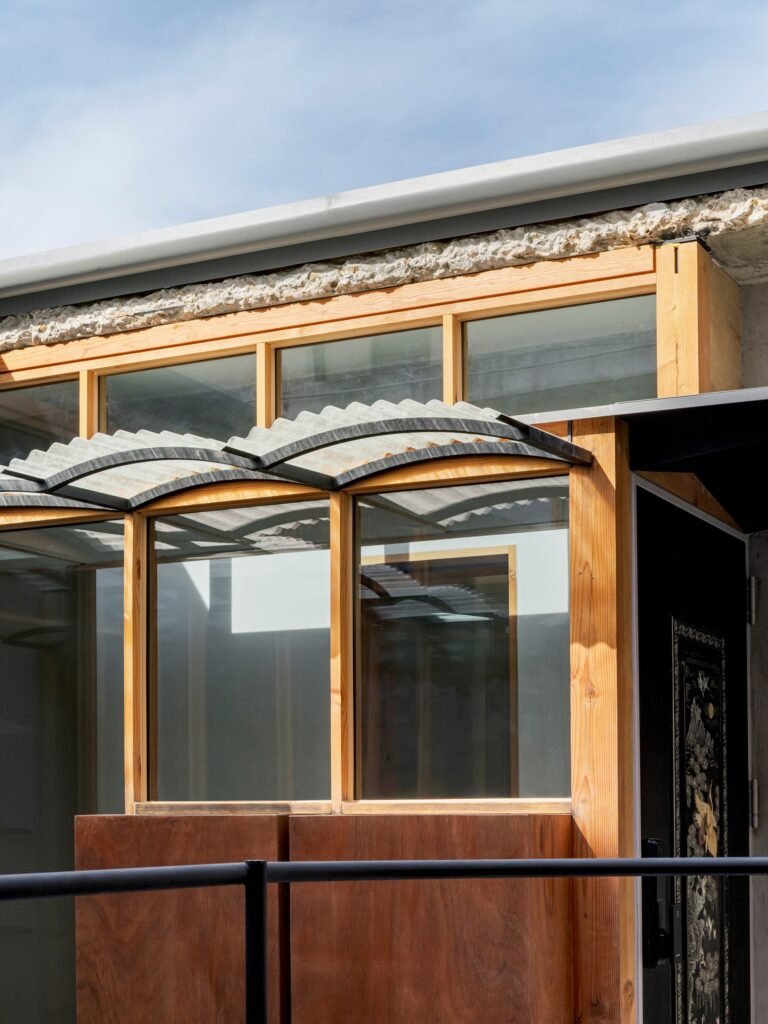 Architectural detail of upper clerestory windows, wooden structural framing, and corrugated translucent FRP canopy at Saekdong House.