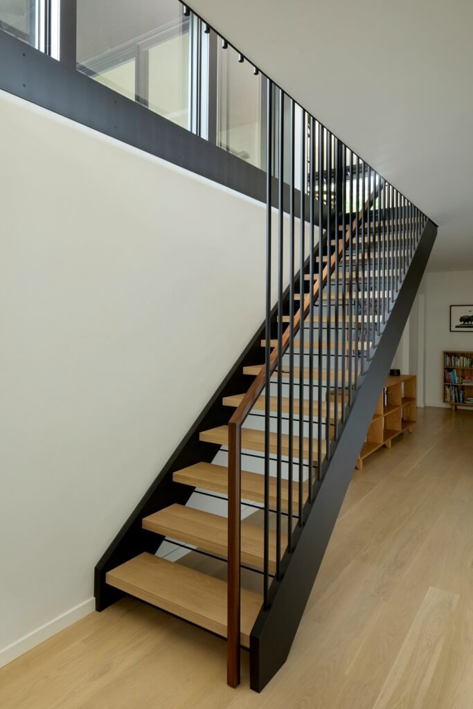Open-riser wood staircase with black steel stringers and thin vertical metal balusters inside the renovated main residence.