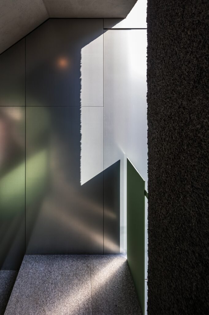 Natural sunlight casting geometric shadows across metallic walls and green door in the stairwell area.