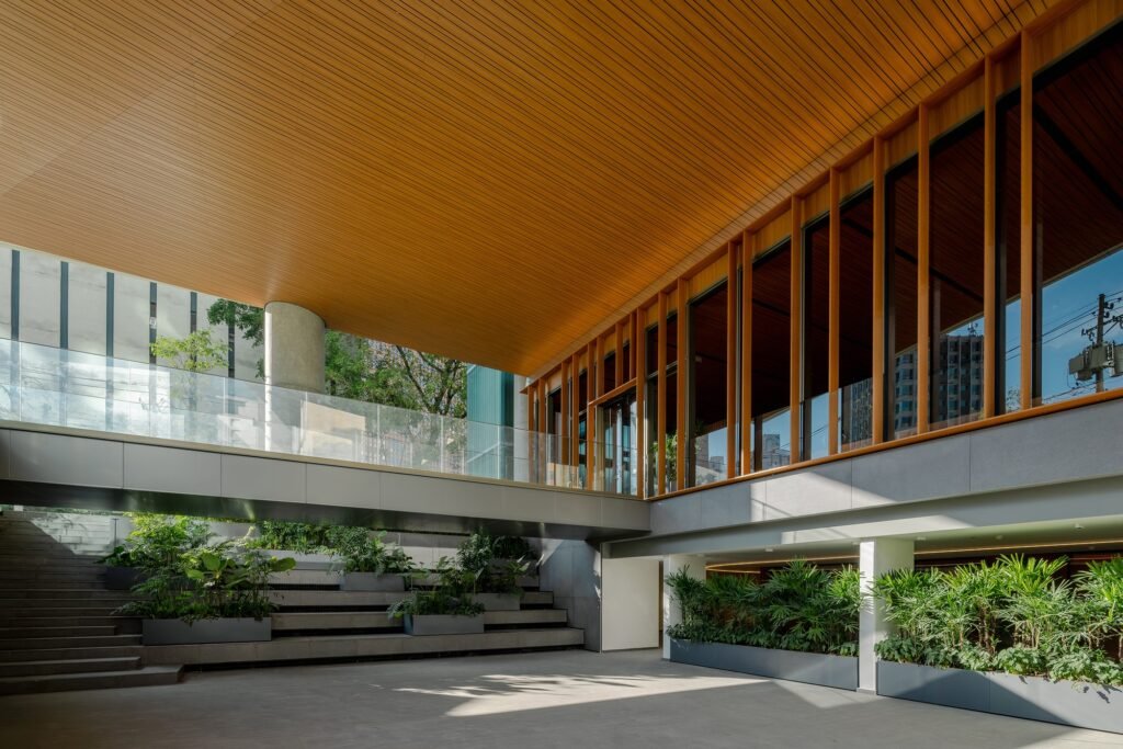 View of the sunken courtyard plaza with terraced planters, concrete steps, and an overhead pedestrian bridge leading to the main building entrance.