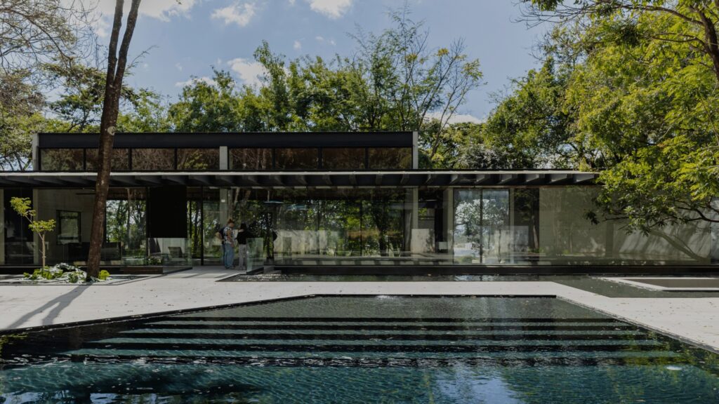 Outdoor swimming pool and glass-enclosed social pavilion in a forested courtyard.