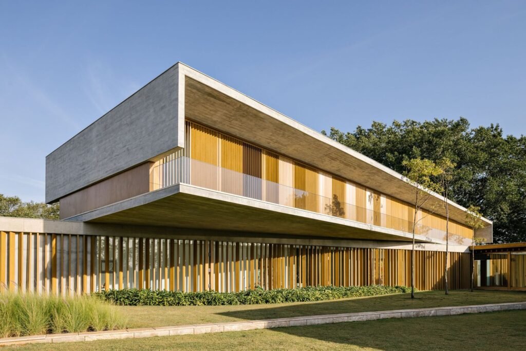 Upper-floor concrete box cantilevered over ground-level wooden louvers at Fazenda Boa Vista.