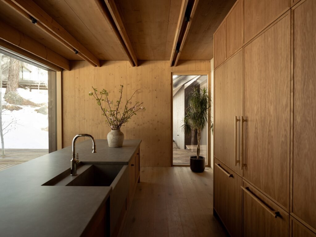 Modern kitchen interior featuring exposed cross-laminated timber ceiling, wood cabinetry, and concrete island.