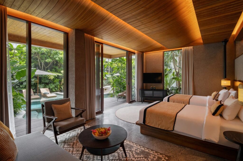 Deluxe double bedroom at Kemilu Ubud with curved timber ceiling, lounge seating, and sliding glass doors opening directly to a private pool.