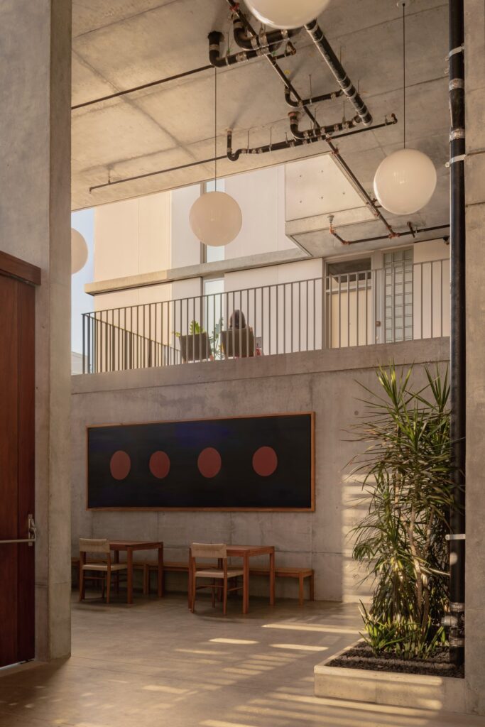 Semi-outdoor seating space in KAYA with exposed concrete ceiling, industrial piping, and views toward upper open walkways.