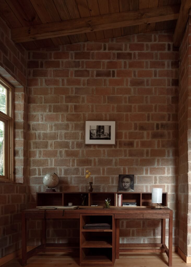 Home office workspace inside Casa Esteli featuring a wooden desk against a red brick wall built in a rat-trap bond pattern.