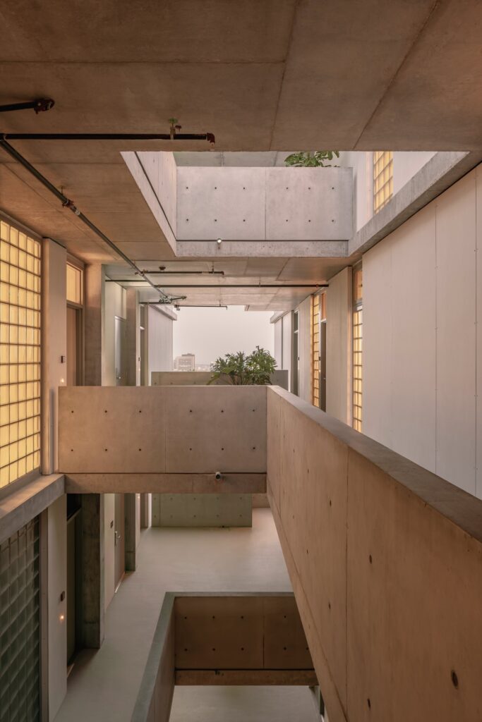 Multi-level open-air walkway in KAYA with concrete parapets, glass block walls, and skylight cutouts bringing light to corridors.