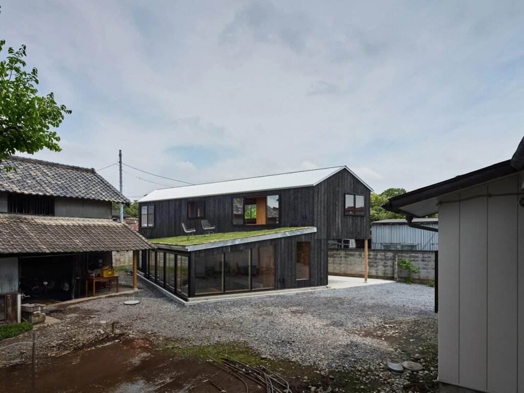 Wide outdoor perspective of House in Mibu within the ancestral family property surrounded by older structures and a gravel yard.