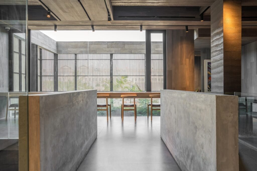 Cafe seating area with raw concrete half-walls facing a full glass fa&ccedil;ade with vertical slatted screens outside.