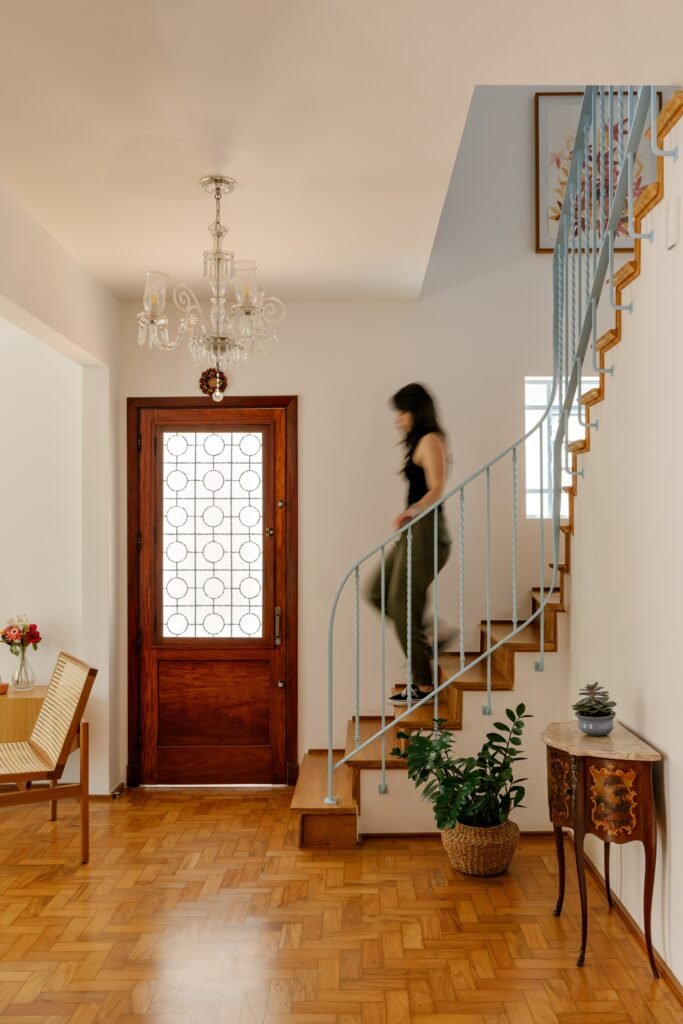 Person walking down a restored Peroba-do-campo wooden staircase with light blue metal railing in Casa M.