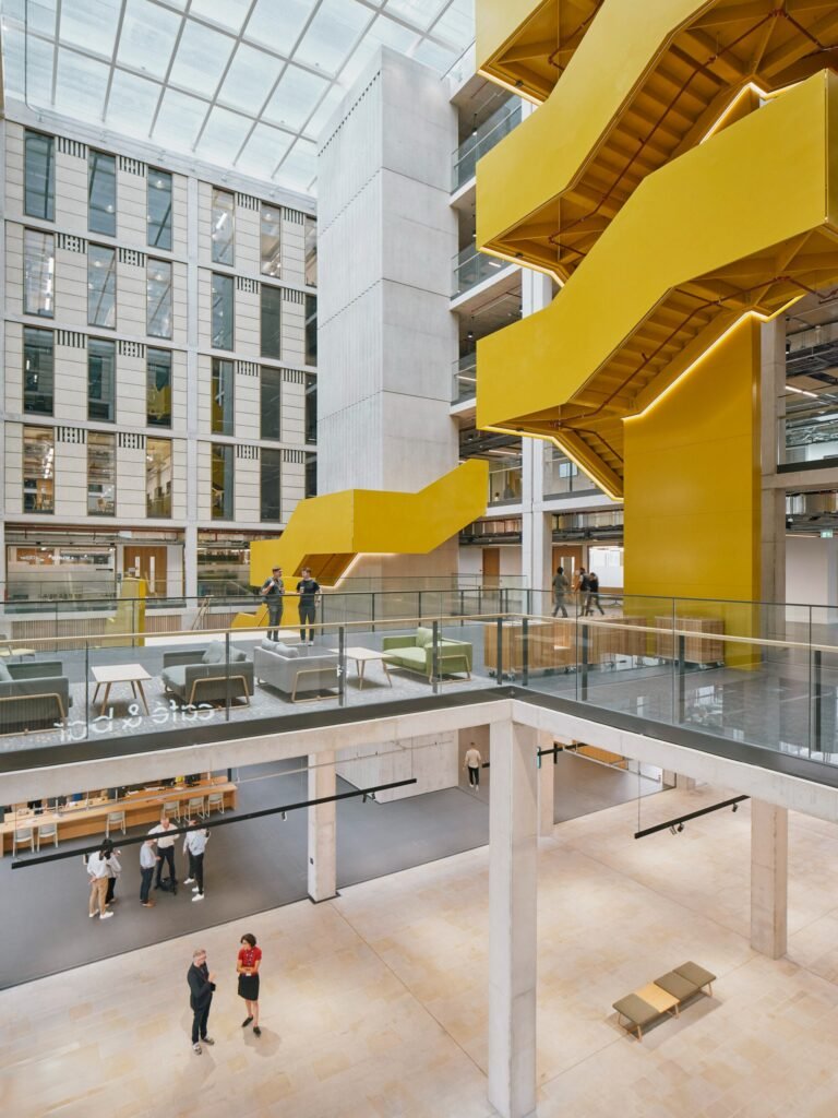 High-ceiling main interior hall with prominent yellow sculptural staircase and public Exchange Hall at ground floor.