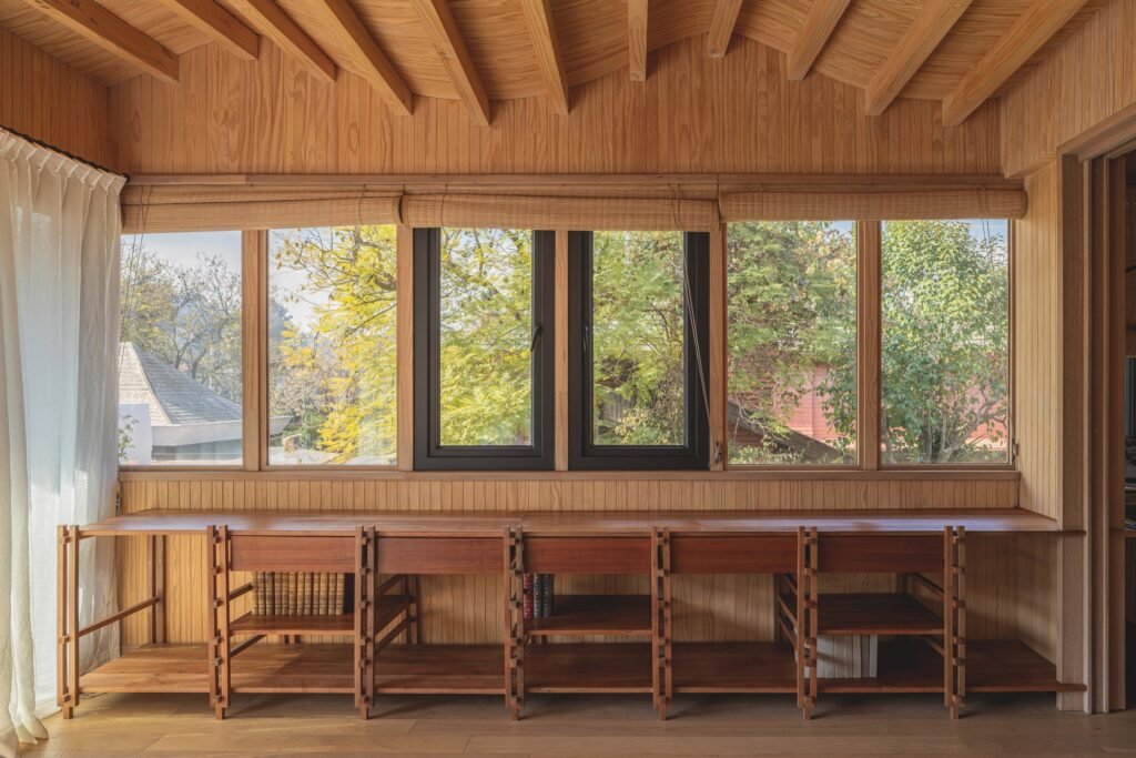Long built-in wooden desk and shelving under a continuous horizontal window frame with exposed rafters above.