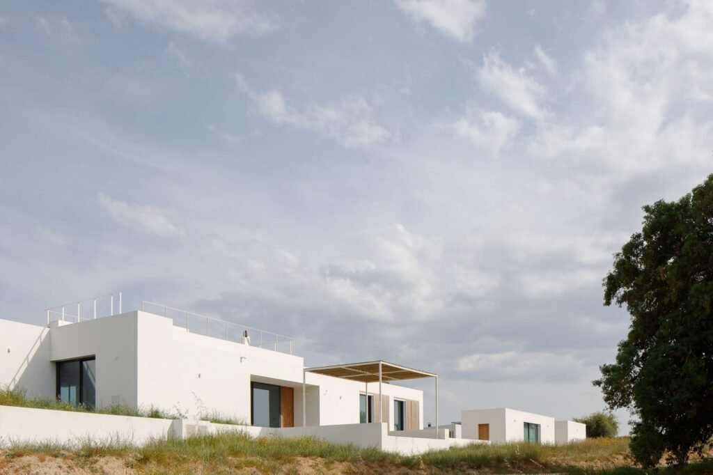 Stepped white building volumes of Melides MG House following the sloping hill terrain.