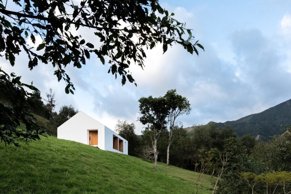 Casa Florinda viewed from a lower grassy slope framed by tree branches under a cloudy sky.