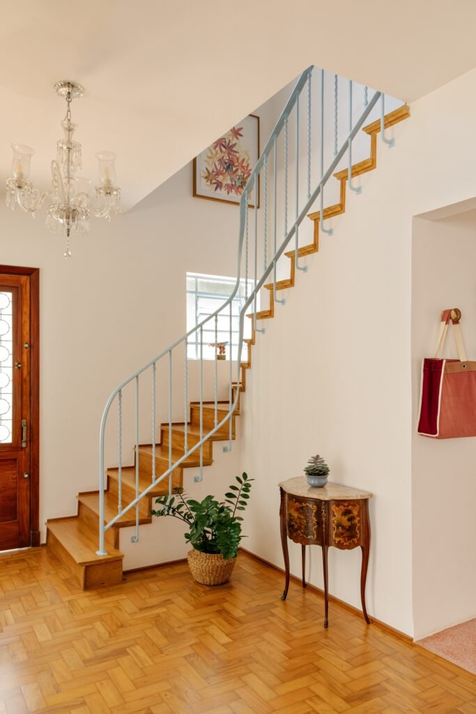 Restored wooden staircase with curved light blue iron balustrade, wooden parquet floors, and decorative vintage furniture.