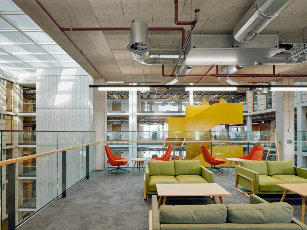 Interior seating lounge overlooking the atrium with visible overhead exposed MEP ducts and timber acoustic ceiling.
