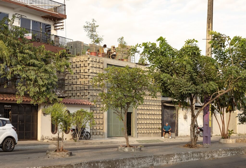 Exterior golden hour view of La Colmena in Dur&aacute;n, Ecuador, showcasing its textured concrete block facade, rooftop gardens, and active street connection on a residential street.