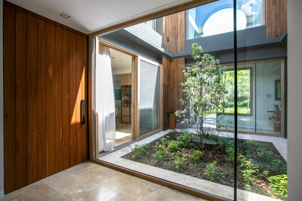 Main entry hall with a large wooden door and floor-to-ceiling glass wall framing an inner courtyard garden with a growing tree.