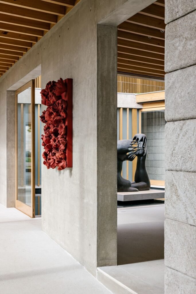 Interior concrete hallway featuring a red wall sculpture and a courtyard view with a black sculpture.