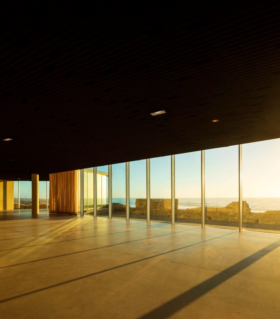 Interior view of the flexible open event hall inside Cresmina Fort with polished concrete floors and floor-to-ceiling glass windows framed by golden sunset light.