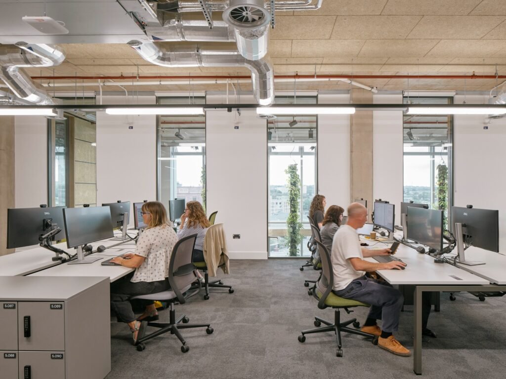 Office and research workspace with rows of computer monitors, workstations, and large windows with green climbing plants.
